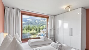 Une chambre d’hôtel avec un grand lit, du linge de lit blanc, une armoire et une vue sur un paysage montagneux.