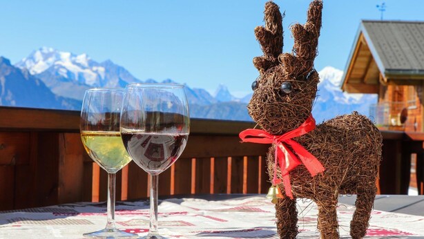 Una figurine di coniglio in vimini con un nastro rosso, due bicchieri da vino e una vista sulle montagne sullo sfondo.