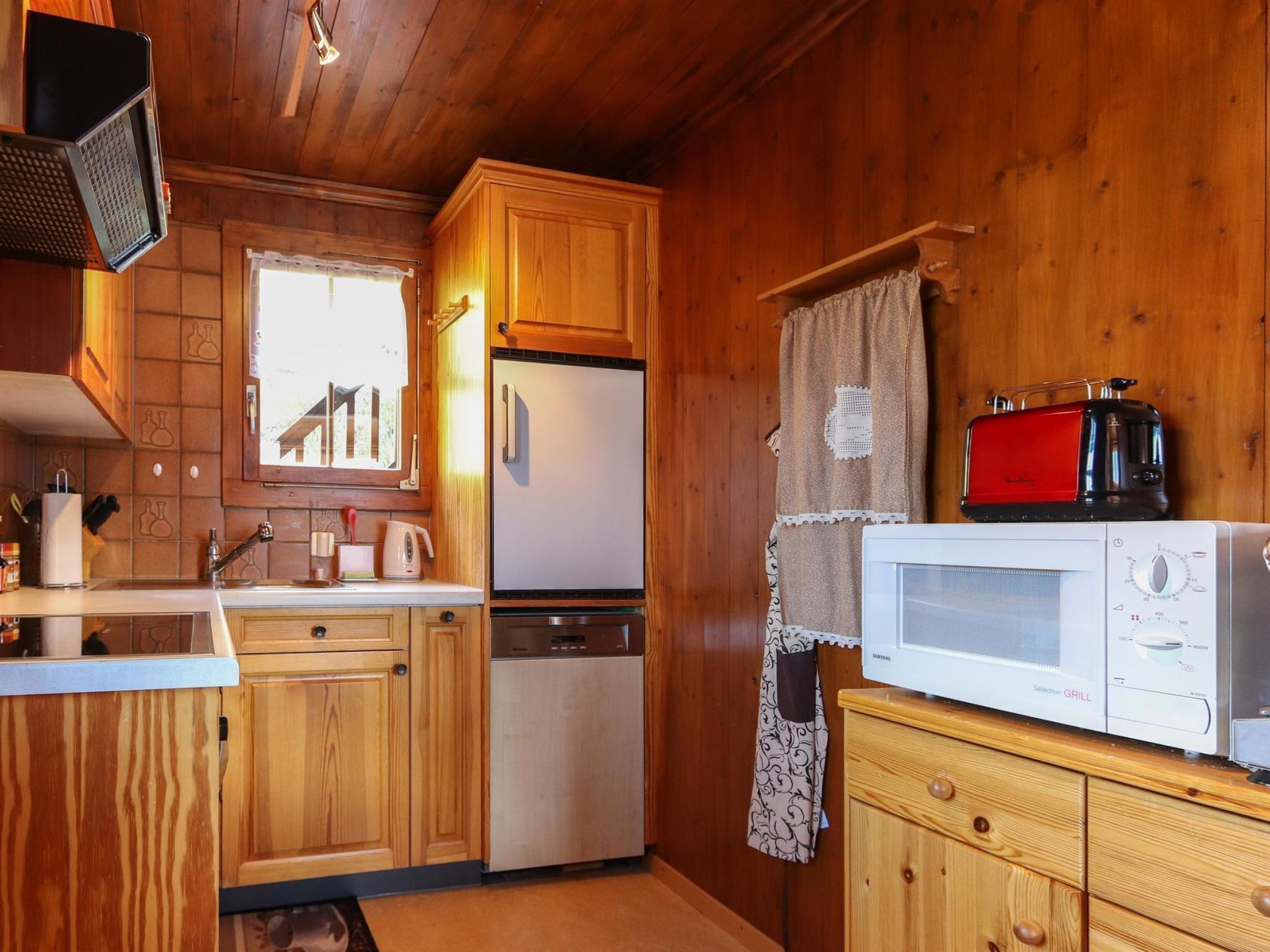 A compact kitchen with wooden cabinets, a refrigerator, a microwave, and a toaster.