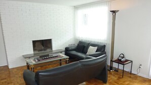 Una sala de estar con pared de ladrillo blanco, chimenea, sofá de cuero negro, mesa de centro y lámpara de pie.