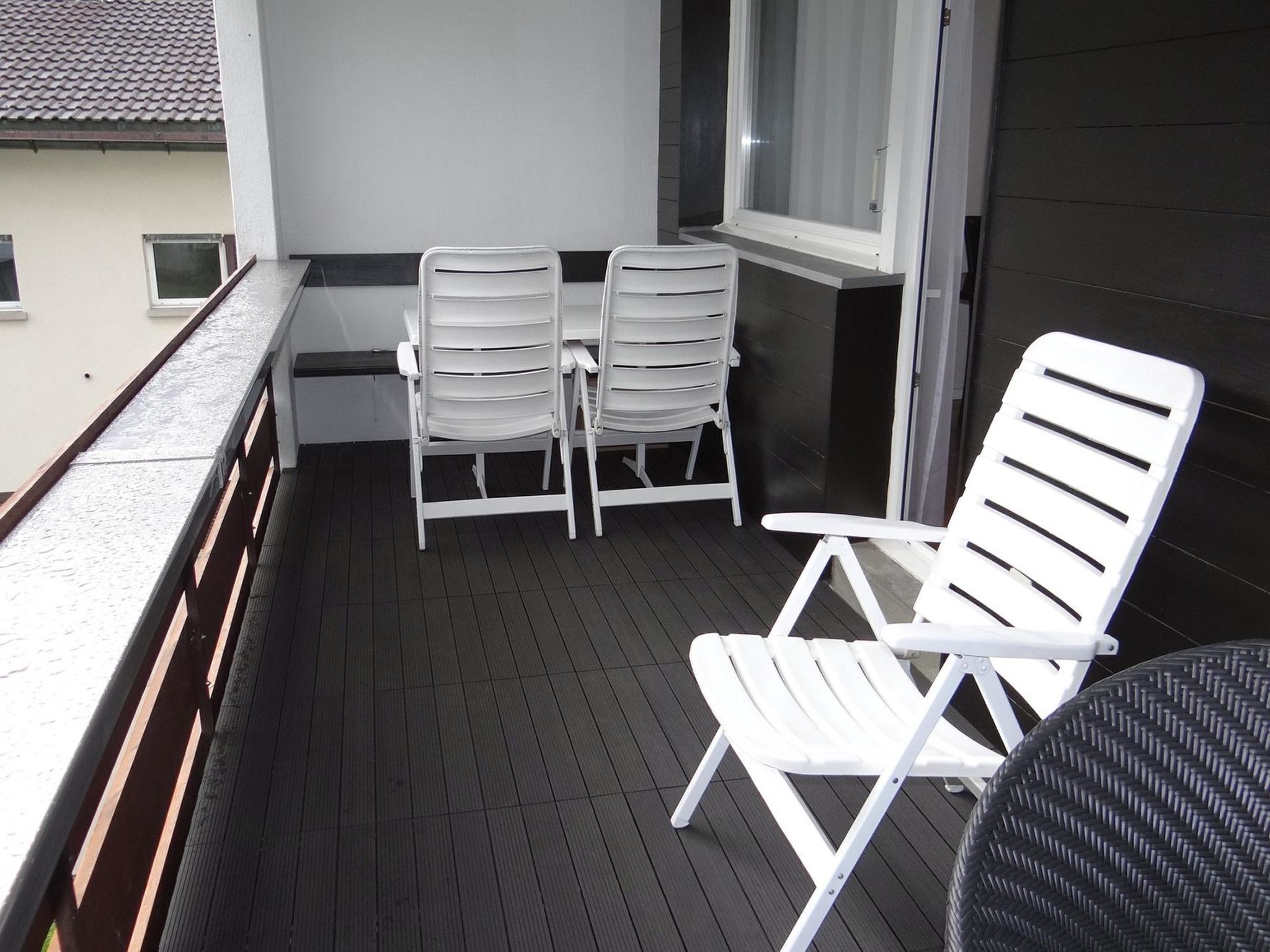 A balcony with a table and two chairs, a window with blinds, and a door.