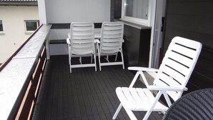 Un balcón con una mesa y dos sillas, una ventana con persianas y una puerta.