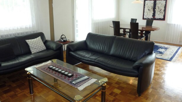 Una sala de estar con dos sofás de cuero negro, una mesa de centro de vidrio y un comedor con mesa y sillas.
