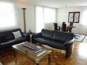Un salon avec deux canapés en cuir noir, une table basse en verre et un coin repas comprenant une table et des chaises.