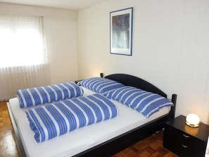 Un letto matrimoniale con lenzuola a righe, un comodino con una lampada e un quadro appeso al muro.