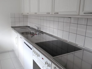 Une cuisine avec des meubles blancs, un évier en acier inoxydable et une plaque de cuisson noire.