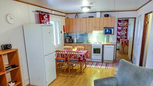 Eine kompakte Küche mit Kühlschrank, Mikrowelle, Herd und Spüle. Im Wohnbereich befindet sich ein Esstisch mit Stühlen sowie eine Couch.