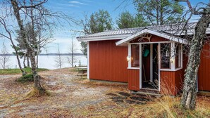 Eine kleine Holzhütte mit einer Tür und einem Fenster, umgeben von Bäumen und einem See.