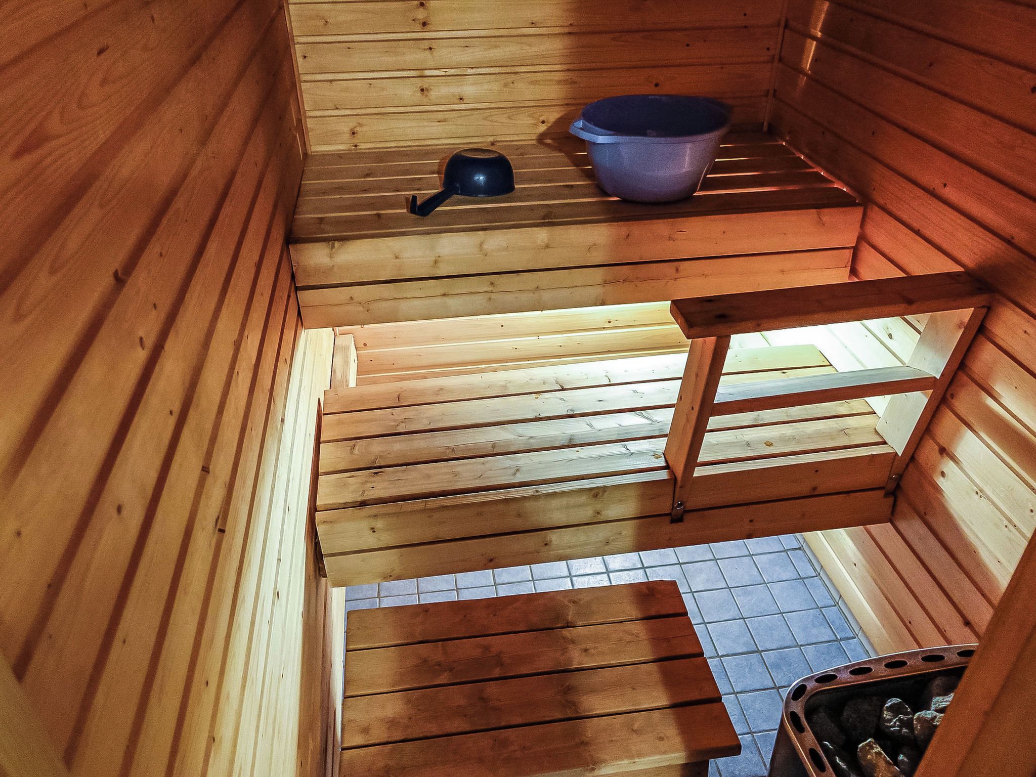 A wooden cabin interior with a sloped ceiling, a metal pot, and a plastic basin on a shelf.