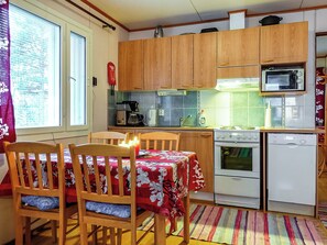 A compact kitchen with wooden cabinets, a microwave, a stove, and a dining table with chairs. - Mellaniemi by Interhome (Inari)