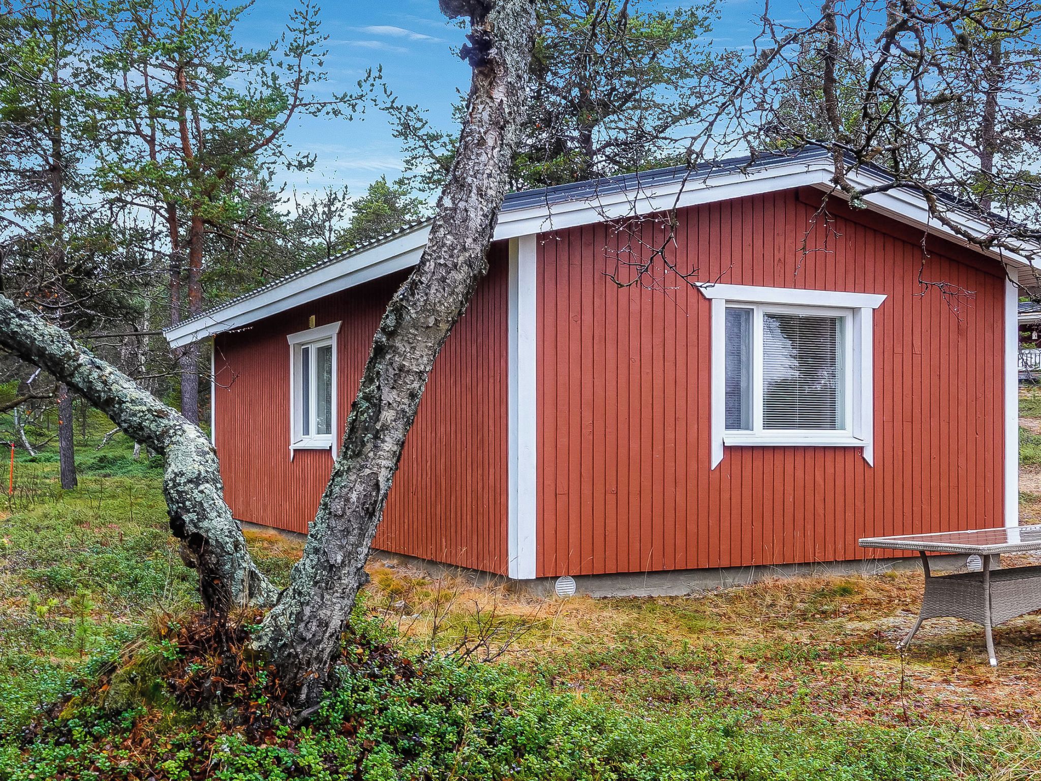 Une cabane en bois rouge, avec une seule fenêtre et une porte, entourée d’arbres et d’herbe.