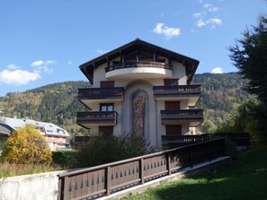 Un immeuble à plusieurs étages doté de balcons, orné d’une statue centrale et ayant une chaîne de montagnes en arrière-plan.