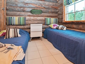 Une chambre de style rustique avec deux lits, une petite commode blanche et une fenêtre donnant sur la forêt.