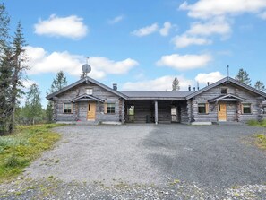 A log cabin with a gravel driveway, two doors, and a chimney.