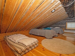 Quarto de sótão pequeno, com telhado inclinado, duas camas, aquecedor e janela.
