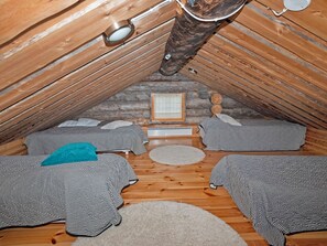 Quarto de sótão acolhedor, com teto inclinado, vigas de madeira, uma pequena janela e uma cama com roupa de cama listrada.