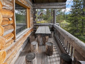 Una cabaña de troncos con terraza de madera, una mesa de picnic y varios taburetes.