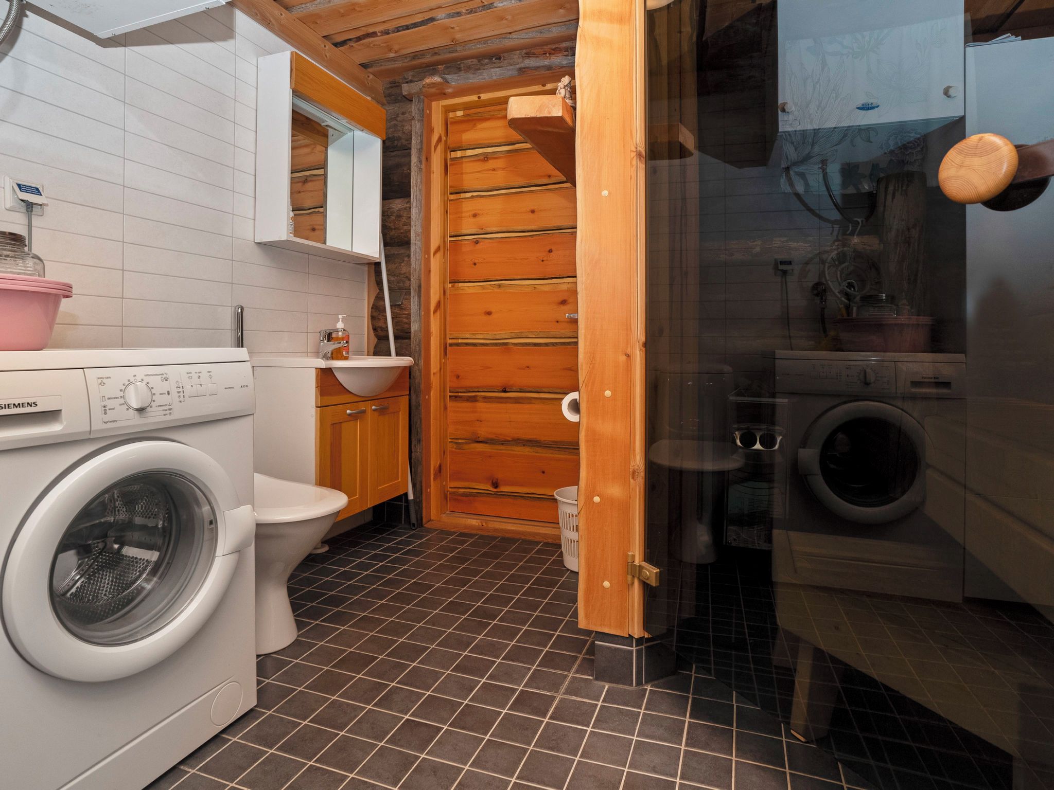 A compact bathroom with a washing machine, toilet, and a wooden door leading to another room.