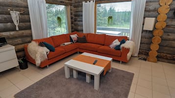 A log cabin interior with a sectional sofa, a small table, and a window with curtains.