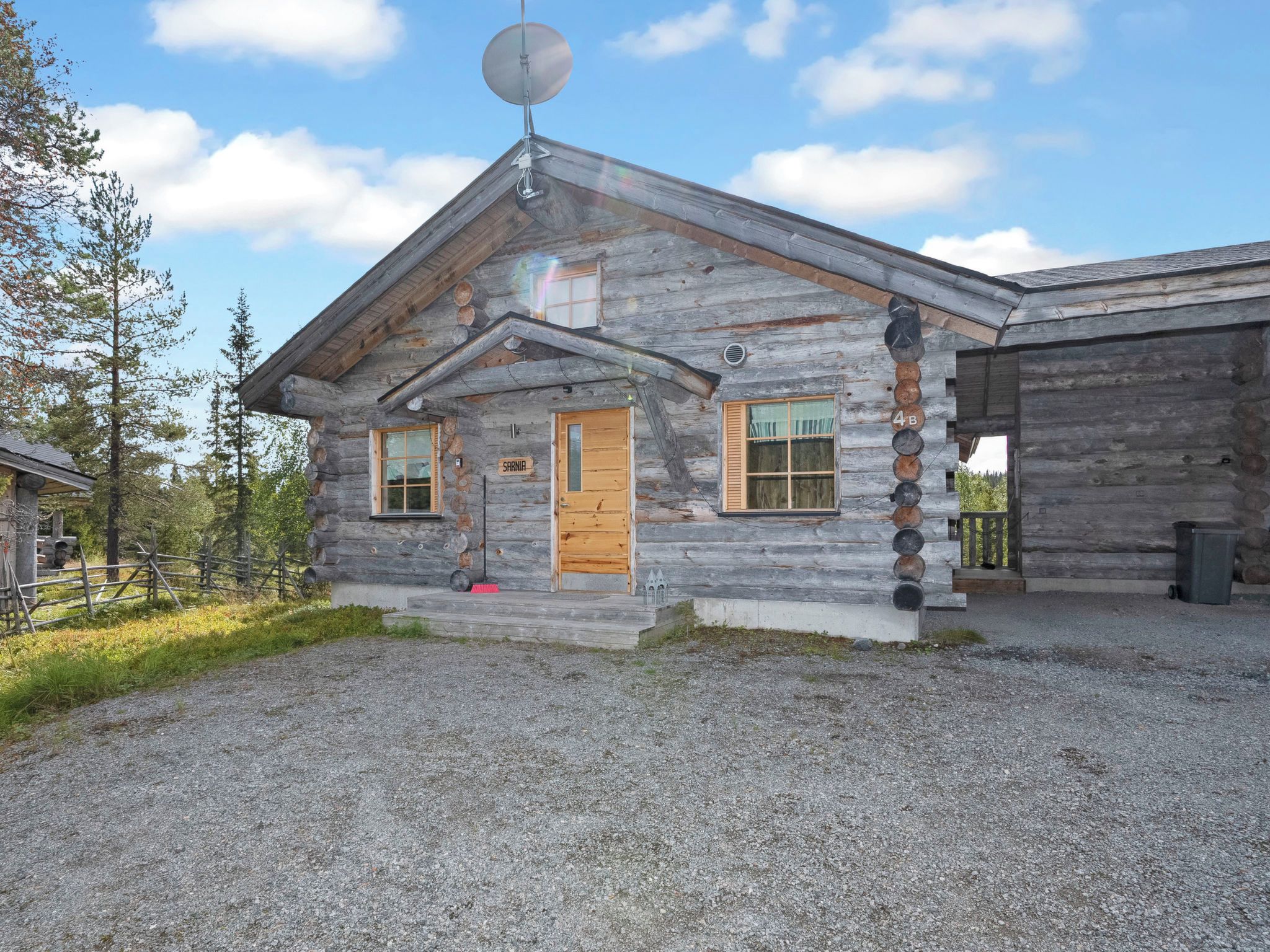 A log cabin with a satellite dish, a wooden door, and a gravel driveway.