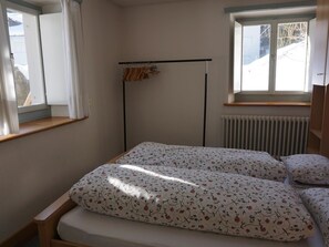A bedroom with a bed, a radiator, a window, and a coat rack.