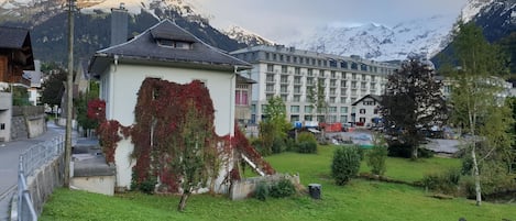 A hotel with a mountain backdrop, a grassy area in front, and a building with ivy.