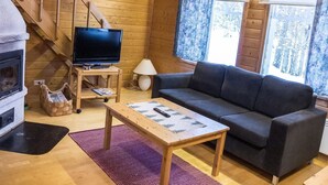 L’intérieur d’un chalet chaleureux, avec un escalier en bois, un téléviseur, un canapé et une cheminée.