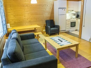 A cozy living room with a sofa, a chair, a small table, and a kitchen area with a refrigerator and stove.