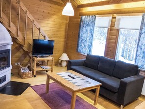 A cozy cabin interior with a wooden interior, a television on a wooden stand, a sofa, a table, and a fireplace.