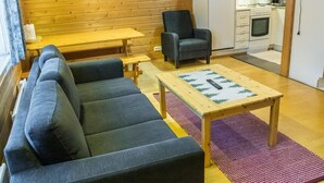 Un salon confortable avec un canapé, un fauteuil, une table en bois et un coin cuisine équipé d’un réfrigérateur et d’une cuisinière.