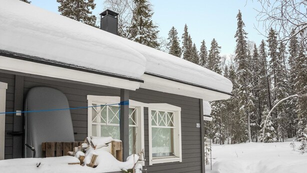 Une cabane dont le toit est recouvert de neige, avec une terrasse en bois et une cheminée.