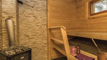 A sauna room with a stone wall, wooden benches, a window, and a steam pipe.