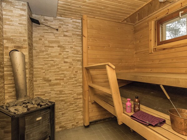 A sauna room with a stone wall, wooden benches, a window, and a steam pipe.