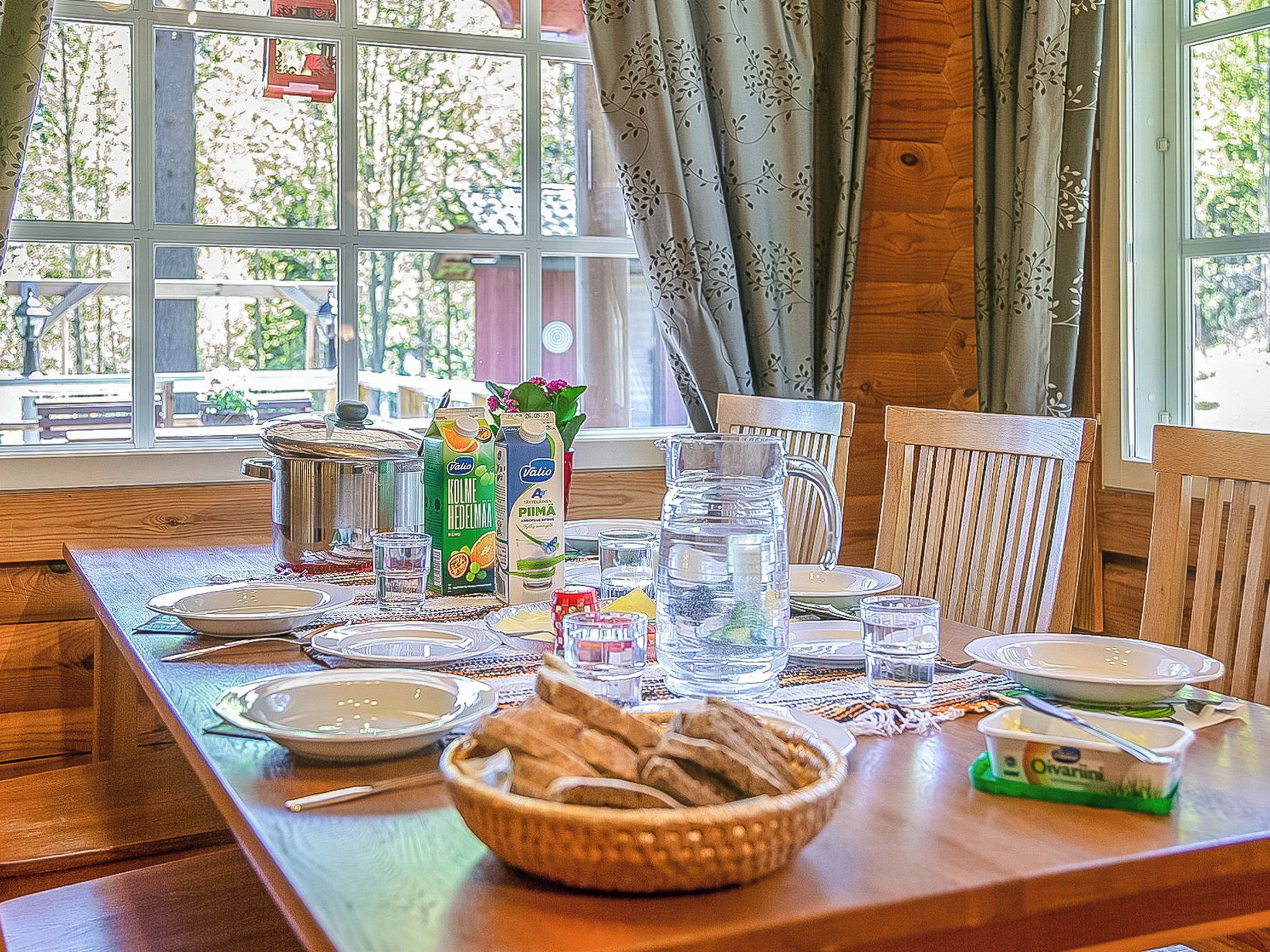 Et spisebord dækket med tallerkener, glas, en kande, en krukke og en skål med brød.