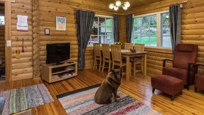 A cozy cabin interior with a wooden interior, a dining table with chairs, a television, and a dog sitting on a rug.