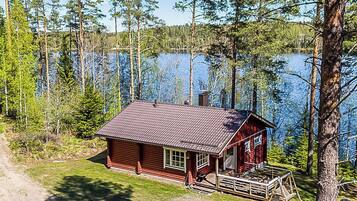 Punakatolla varustettu mökki, jonka ympärillä on puita ja jonka lähellä on järvi.