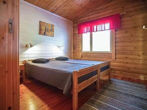 A wooden cabin room with a bed, a window with red curtains, and a painting on the wall. - Kytöranta by Interhome (Hartola)