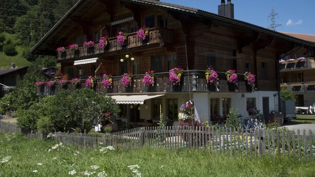A wooden chalet with balconies adorned with flowers, surrounded by a wooden fence and lush greenery. - Steimandli by Interhome (Gstaad)