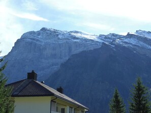 Ein Berg mit schneebedeckten Gipfeln und ein Gebäude mit dunklem Dach im Vordergrund.