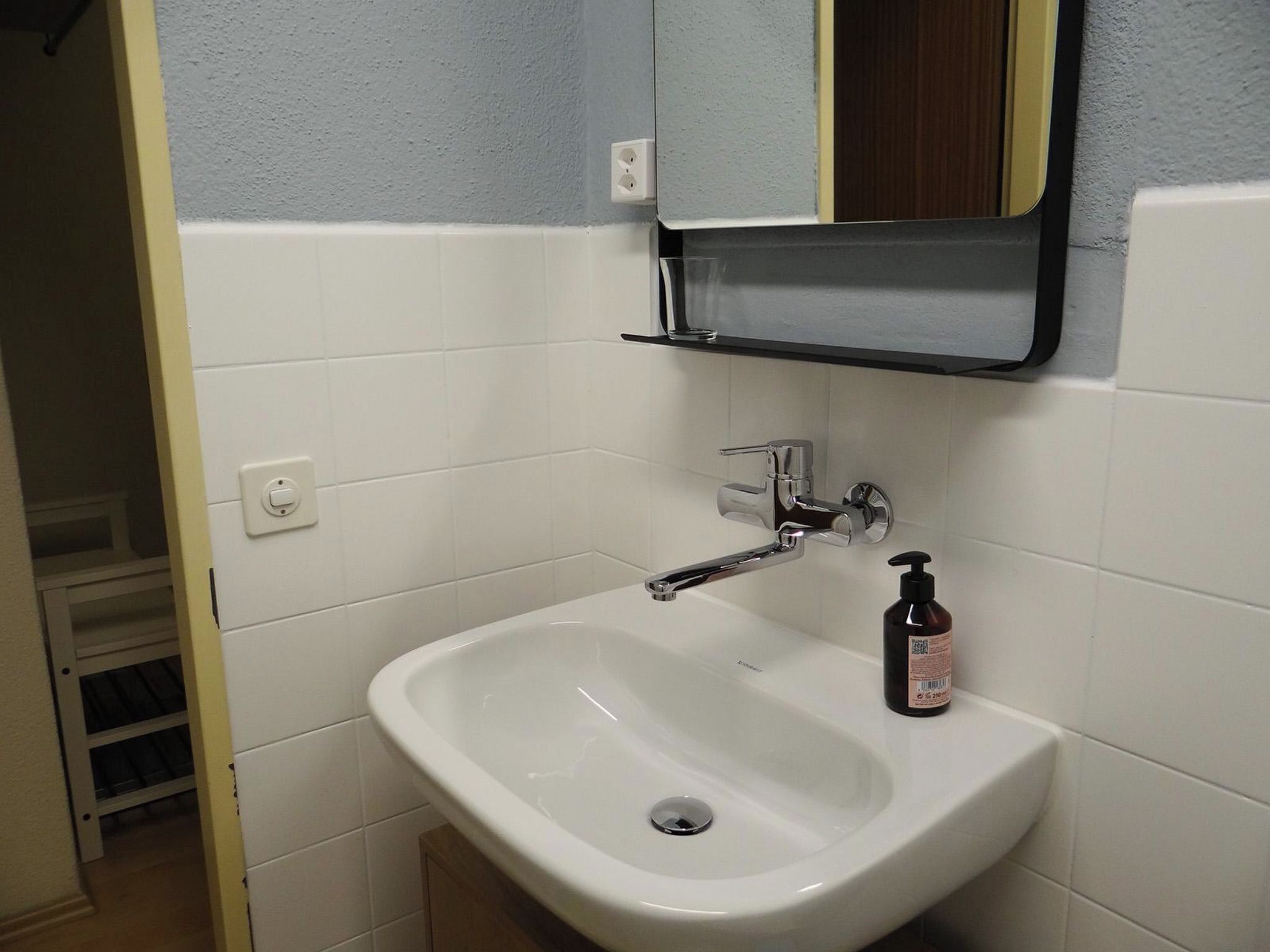 A bathroom with a white sink, a mirror above it, and a bottle of soap on the sink's edge.
