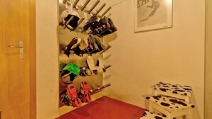 A room with a red carpet, a door, a wall-mounted rack with helmets and ski gear, and a framed picture of a skier. - Apartment Maria by Interhome (Saas-Fee)