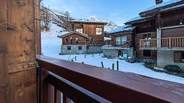 A wooden chalet with stone foundations, a balcony, and a view of snow-covered mountains. - Les Olympiques (Tignes 1800) by Interhome (Tignes)