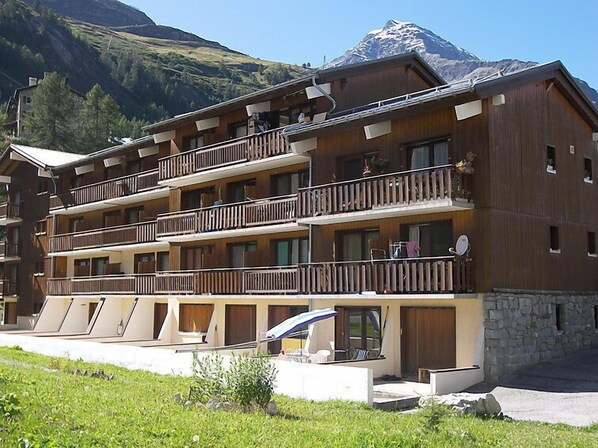 Ein mehrstöckiges Hotel mit Balkonen, einem Steinfundament und einem Berg im Hintergrund.