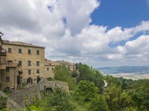 Un bâtiment historique en pierre, doté d’une cour intérieure, entouré d’une végétation luxuriante et offrant une vue imprenable sur une vallée pittoresque.