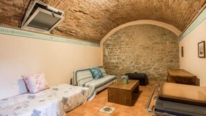 Quarto aconchegante com teto de pedra, sofá com roupa de cama floral, mesa de madeira pequena e um banco.