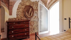 Quarto com parede de pedra, cómoda de madeira, cama e porta deslizante.