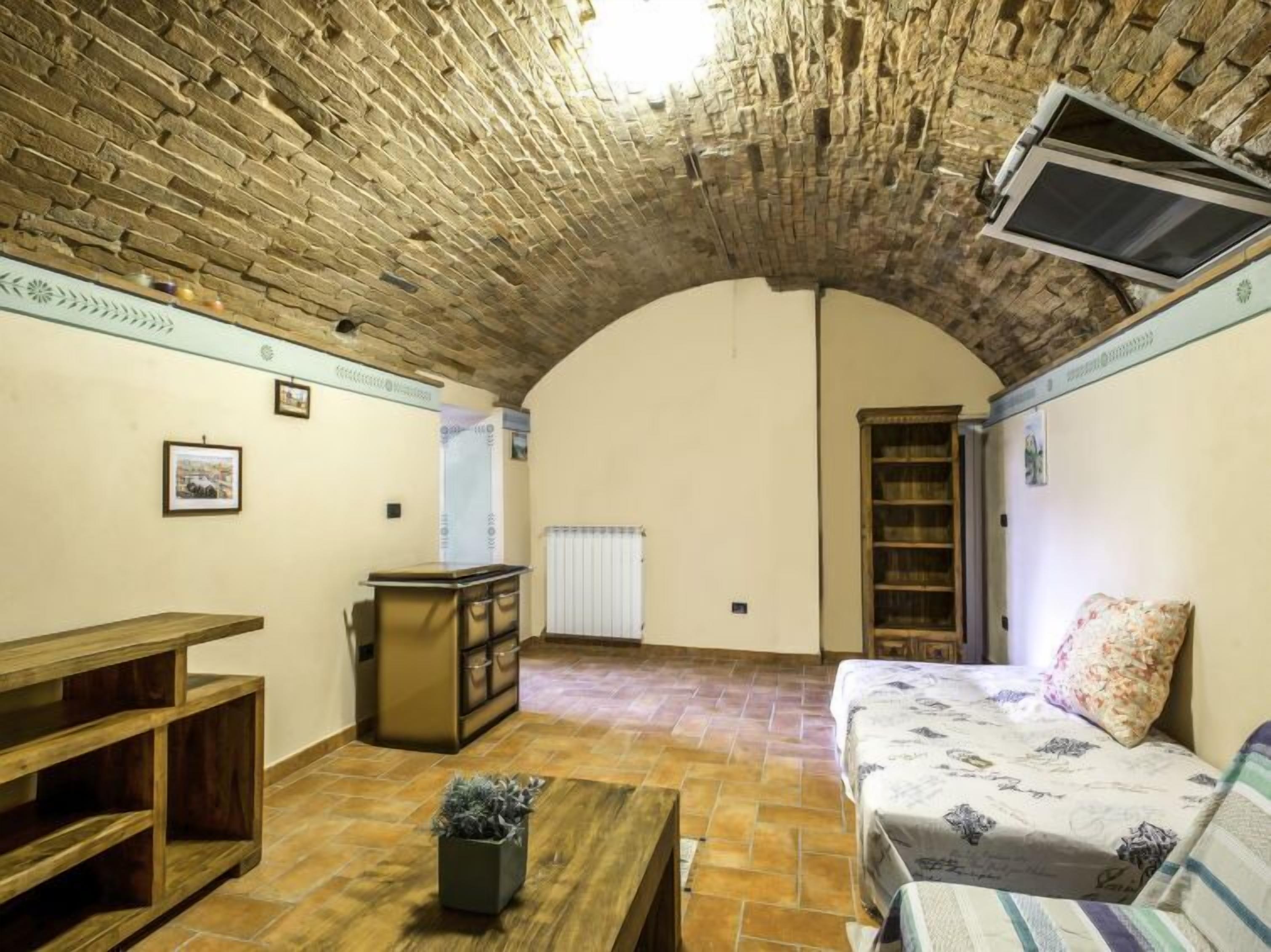Ein rustikales Zimmer mit gewölbter Decke, einer Couch, einem Holztisch, einer kleinen Pflanze und einem Bücherregal.