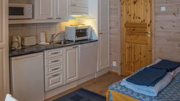 A compact kitchen with a microwave, toaster, and a small oven. There's a wooden door and a bed with a blue and white checkered blanket.