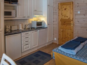 A compact kitchen with a microwave, toaster, and a small oven. There's a wooden door and a bed with a blue and white checkered blanket. - Vaeltajankulma huoneisto 3 by Interhome (Ylläsjärvi)