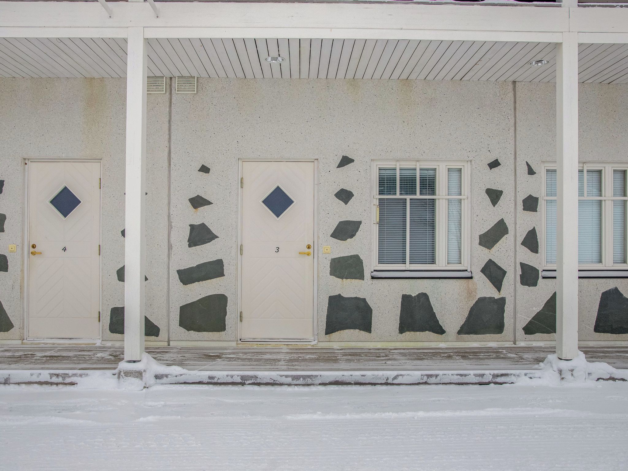 Un bâtiment doté de deux portes, chacune ornée d’une fenêtre en forme de losange, et d’une fenêtre avec des stores horizontaux.